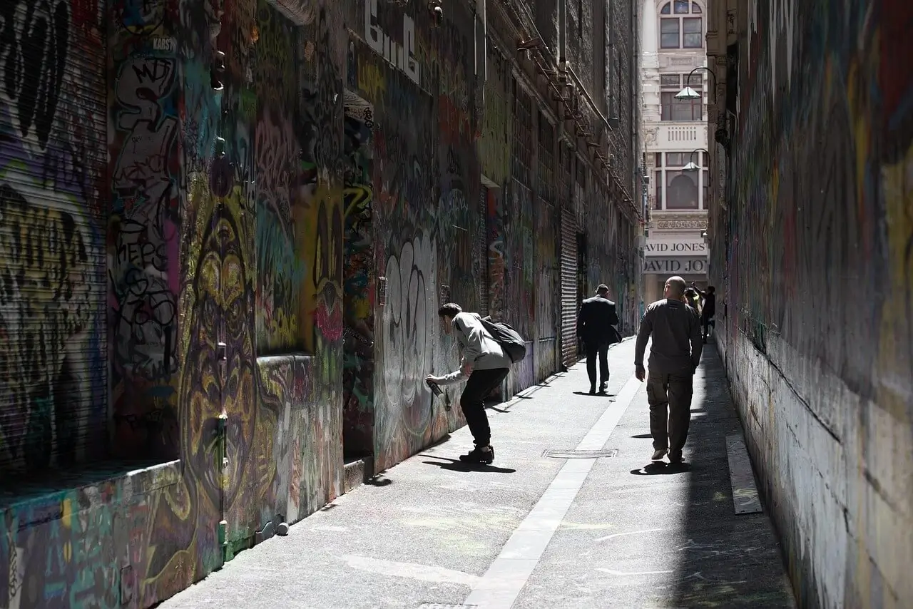 Colorful street art covering laneway walls with people walking through narrow alley