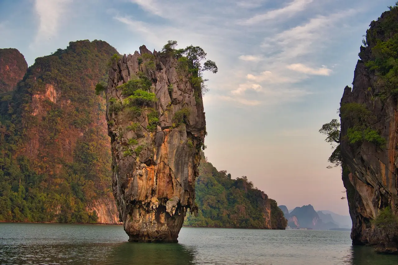 Iconic limestone tower rising dramatically from emerald green water with longtail boats nearby