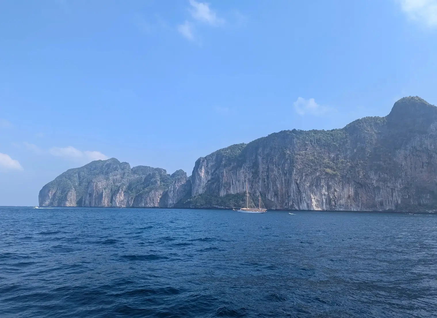 Dramatic limestone cliffs surrounding turquoise bay with longtail boats and white sand beach