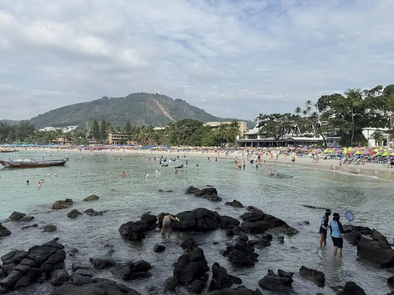 Tropical beach with golden sand, clear blue water, palm trees, and longtail boats